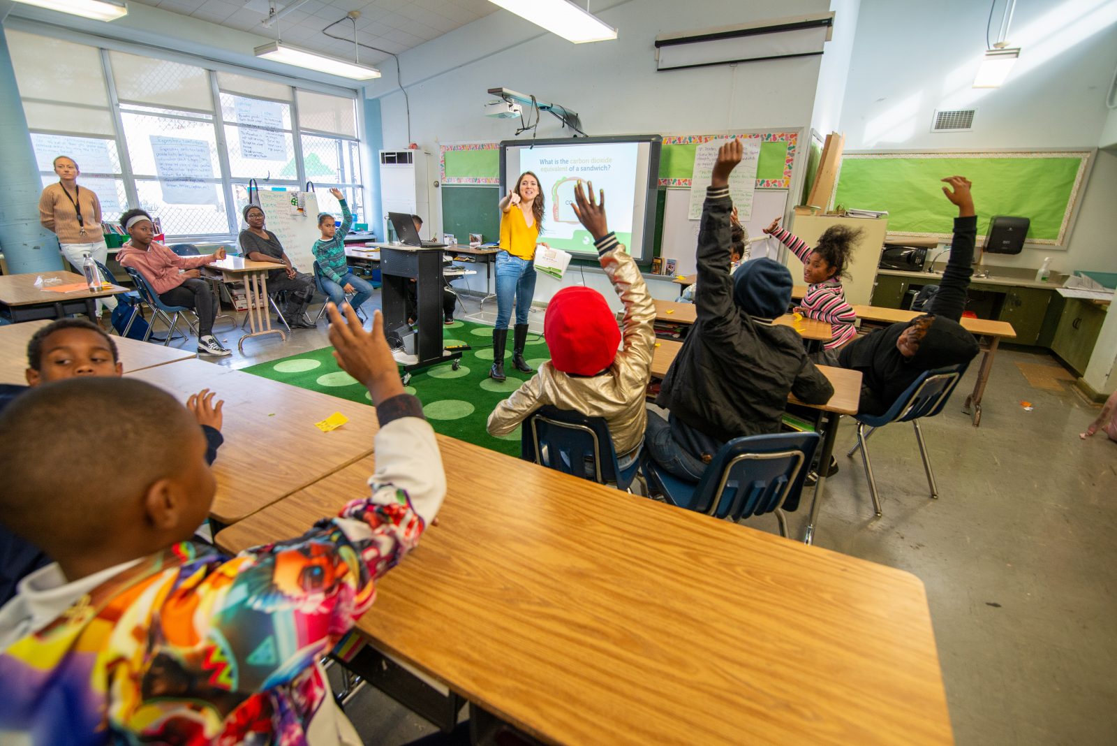 Humane Education Leader in front of a classroom of children with hands raised