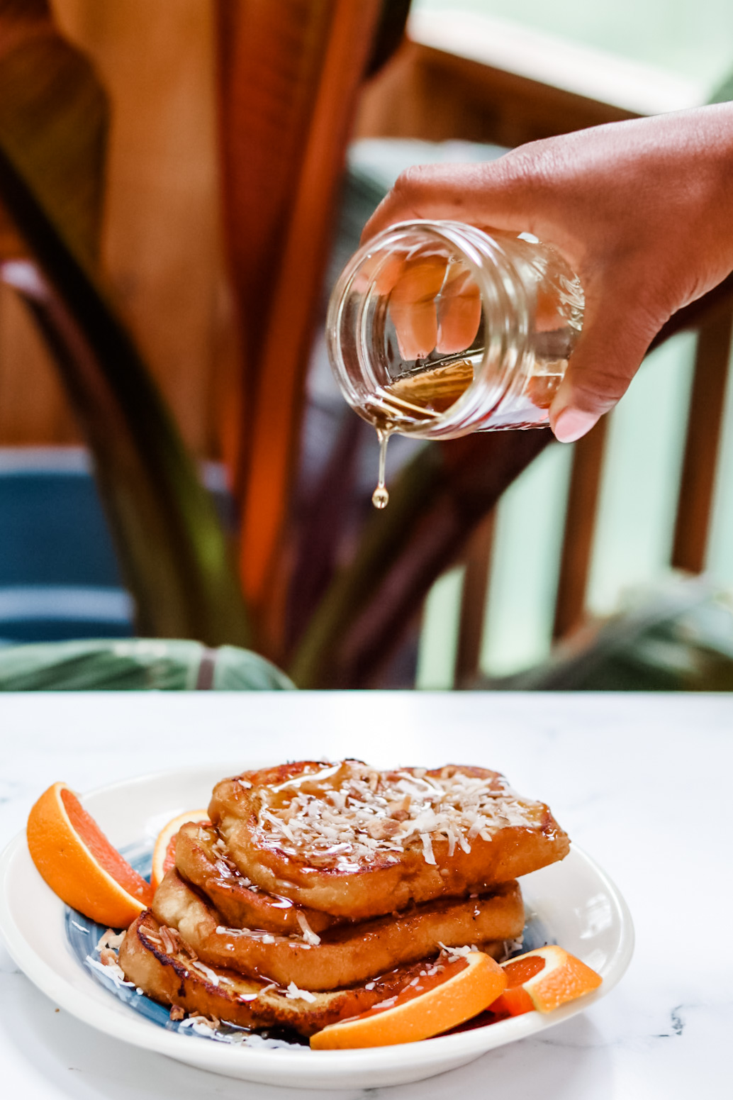 Hand pouring syrup on French toast with coconut and oranges