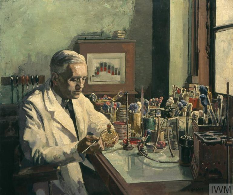 A portrait of Alexander Fleming, wearing a white coat, at work at a desk inside a laboratory. An array of scientific equipment is placed on the surface of the desk and there is a window to the right of the composition.